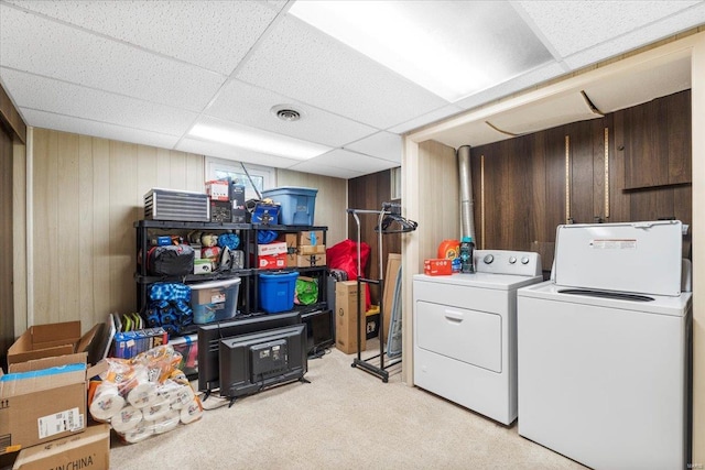 clothes washing area with wooden walls, laundry area, light colored carpet, visible vents, and washer and clothes dryer