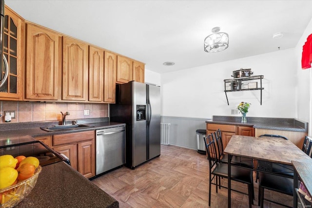 kitchen featuring wainscoting, dark countertops, glass insert cabinets, a sink, and stainless steel appliances
