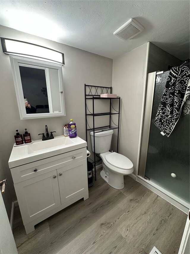 full bathroom featuring vanity, toilet, wood finished floors, visible vents, and a stall shower