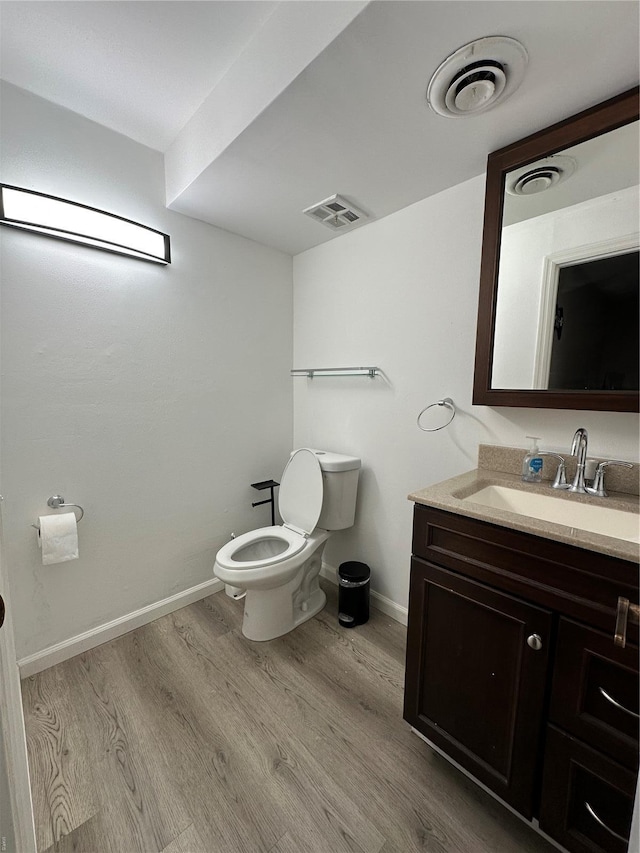 half bath with visible vents, wood finished floors, vanity, baseboards, and toilet