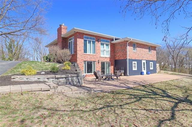 rear view of property with brick siding, a chimney, a patio area, a yard, and a fire pit