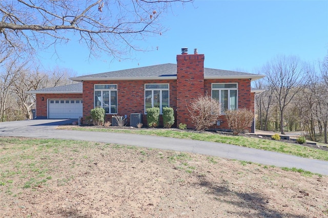 ranch-style house with an attached garage, brick siding, a chimney, cooling unit, and driveway
