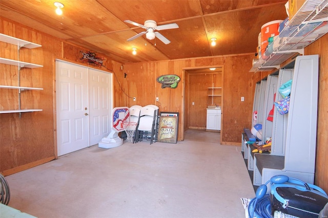 interior space featuring ceiling fan, wood walls, and concrete floors