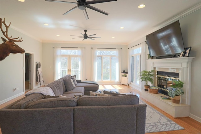 living room featuring crown molding, a ceiling fan, a premium fireplace, and light wood-style floors