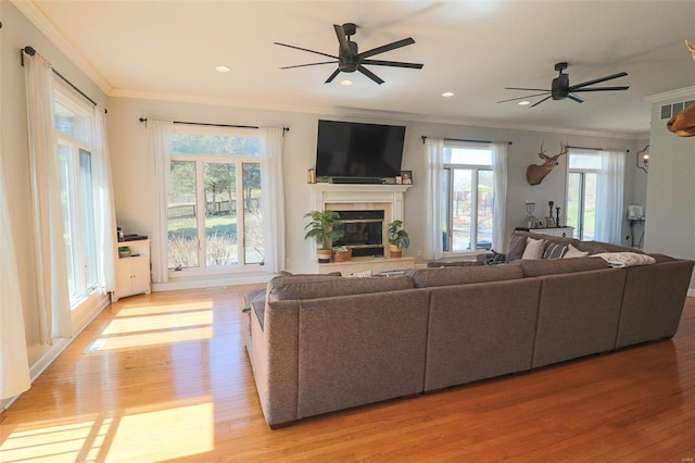 living room featuring crown molding, a glass covered fireplace, light wood-style floors, ceiling fan, and recessed lighting