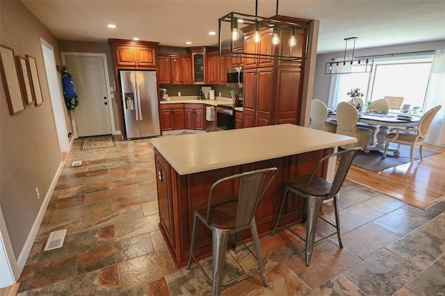 kitchen with brown cabinetry, stainless steel appliances, baseboards, visible vents, and stone tile flooring