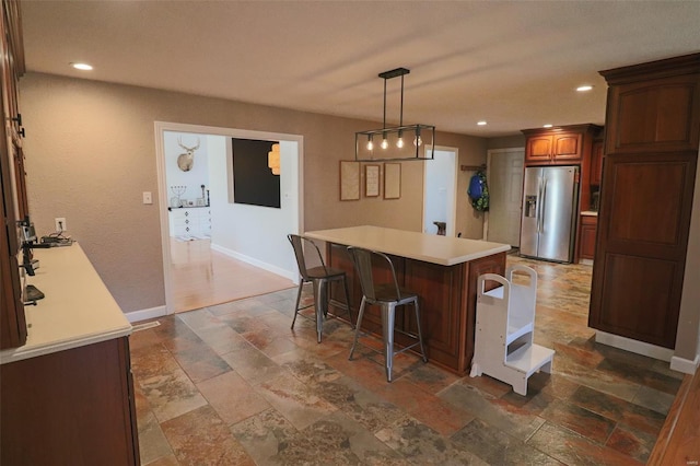 kitchen featuring stone tile flooring, a breakfast bar, baseboards, light countertops, and stainless steel fridge with ice dispenser