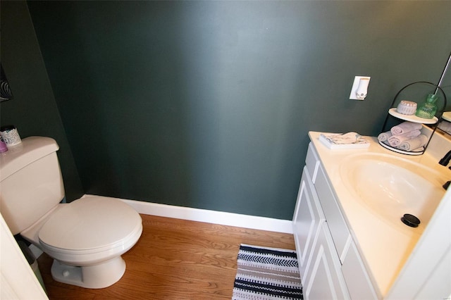 half bathroom with baseboards, wood finished floors, toilet, and vanity