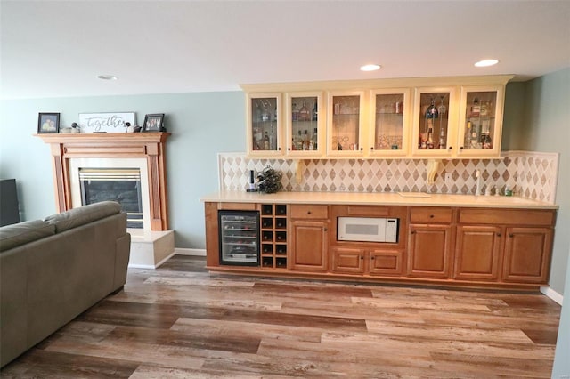bar featuring backsplash, beverage cooler, light wood-style flooring, and white microwave