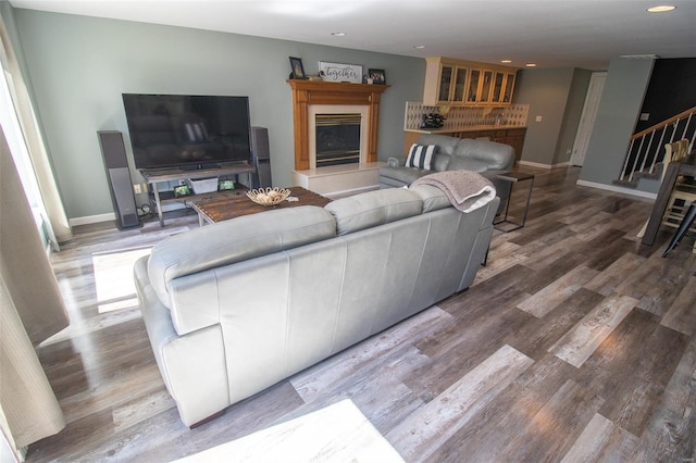 living room featuring baseboards, a fireplace with raised hearth, wood finished floors, and stairway