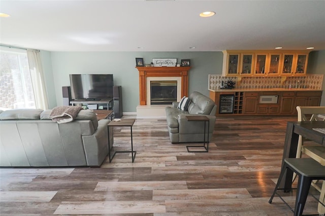 living area featuring a glass covered fireplace, recessed lighting, wood finished floors, and wine cooler