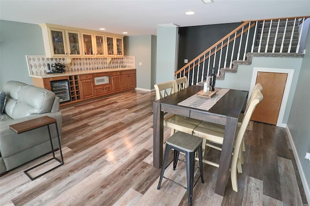 dining room featuring light wood finished floors, stairs, baseboards, wine cooler, and a bar