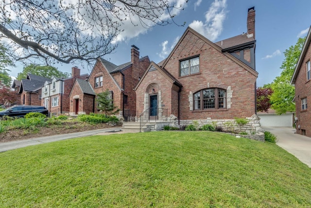 tudor house with brick siding, a chimney, and a front lawn