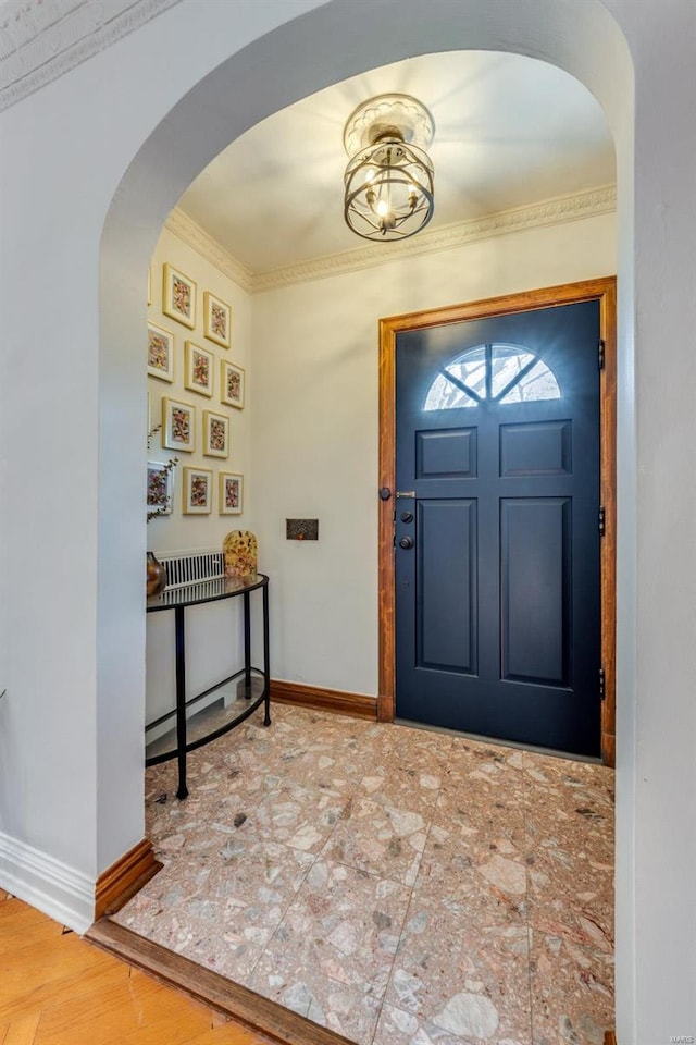 foyer entrance with crown molding, arched walkways, and baseboards