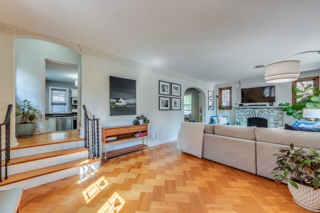 living room featuring a stone fireplace, arched walkways, a wealth of natural light, and stairway