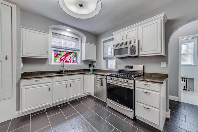 kitchen with arched walkways, a sink, baseboards, white cabinets, and stainless steel appliances
