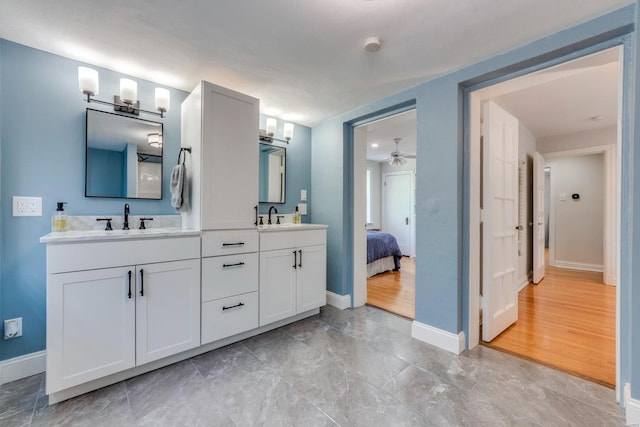 ensuite bathroom featuring baseboards, ceiling fan, and a sink