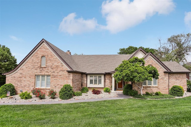 ranch-style home with brick siding, roof with shingles, a chimney, and a front yard