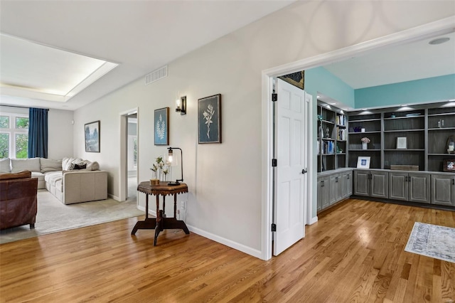 hall featuring baseboards, light wood finished floors, and visible vents