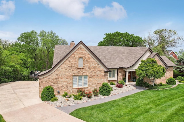 view of front of home with a chimney, brick siding, roof with shingles, and a front lawn