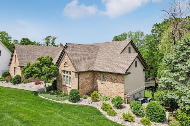 view of home's exterior featuring roof with shingles, a chimney, brick siding, and a lawn