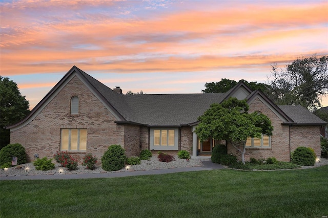 view of front of house featuring a lawn, a chimney, roof with shingles, and brick siding