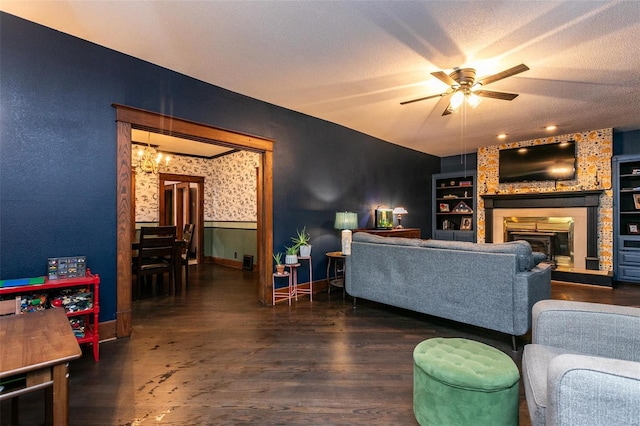living room featuring built in shelves, wood finished floors, baseboards, ceiling fan with notable chandelier, and a glass covered fireplace