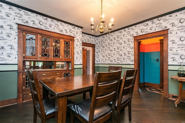 dining space featuring crown molding, dark wood finished floors, a wainscoted wall, an inviting chandelier, and wallpapered walls