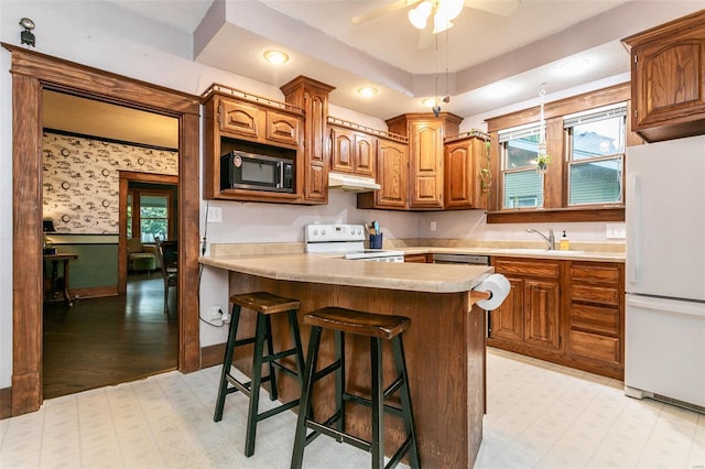 kitchen with white appliances, light floors, light countertops, under cabinet range hood, and a sink