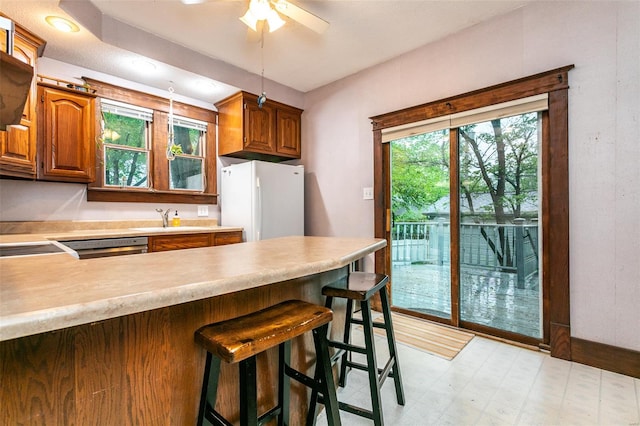 kitchen with brown cabinetry, freestanding refrigerator, a peninsula, a kitchen breakfast bar, and light countertops