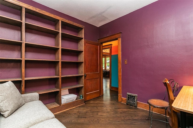 interior space featuring baseboards, visible vents, a textured wall, and dark wood-type flooring