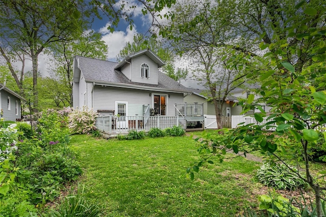 rear view of property with fence, roof with shingles, a wooden deck, a gate, and a lawn
