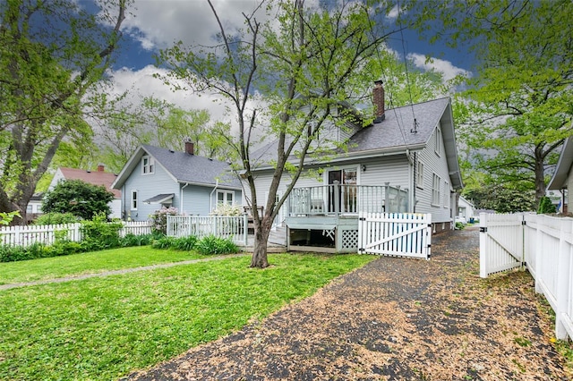 view of front of house featuring a wooden deck, a front yard, a fenced backyard, a gate, and a chimney