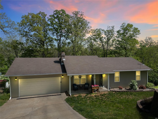 single story home with a garage, a chimney, a lawn, driveway, and a porch