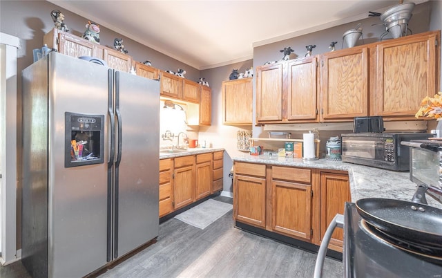 kitchen with a sink, black microwave, crown molding, stainless steel refrigerator with ice dispenser, and light wood-type flooring