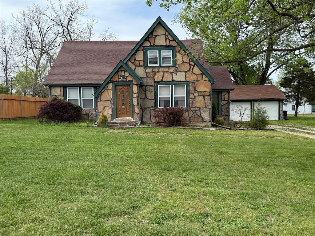 tudor house with fence, roof with shingles, a front lawn, and stone siding
