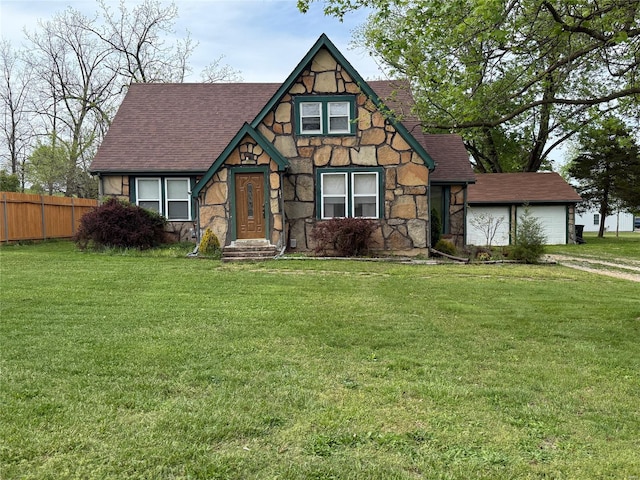tudor house with fence, roof with shingles, a front lawn, and stone siding