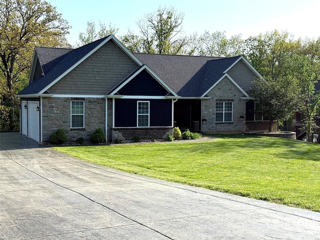 view of front of property featuring a garage, stone siding, driveway, and a front yard