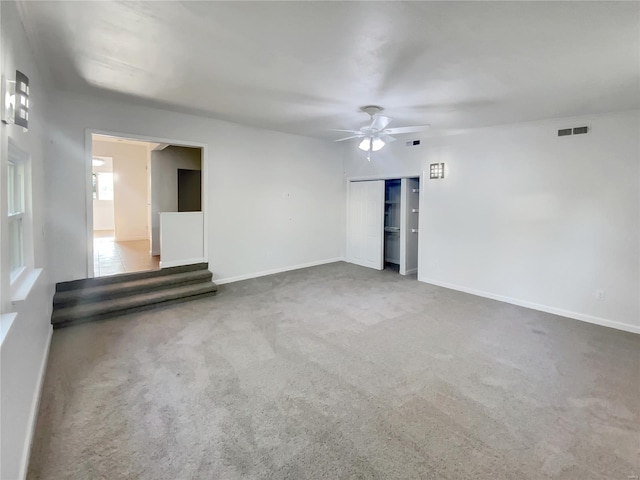 carpeted empty room with stairs, ceiling fan, visible vents, and baseboards