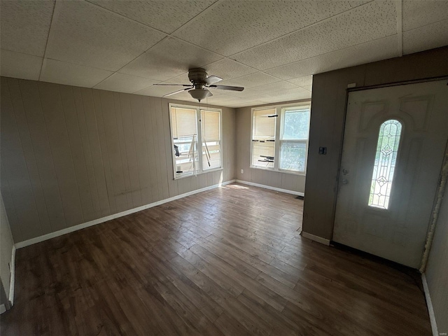 entryway featuring ceiling fan, wood walls, dark wood finished floors, baseboards, and a drop ceiling