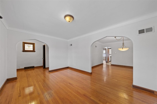 empty room with arched walkways, visible vents, and light wood-type flooring