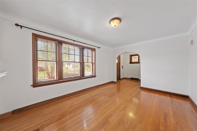 unfurnished room with arched walkways, plenty of natural light, baseboards, and light wood-type flooring