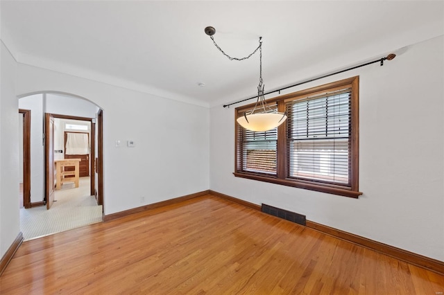 unfurnished dining area featuring arched walkways, baseboards, visible vents, and light wood-type flooring