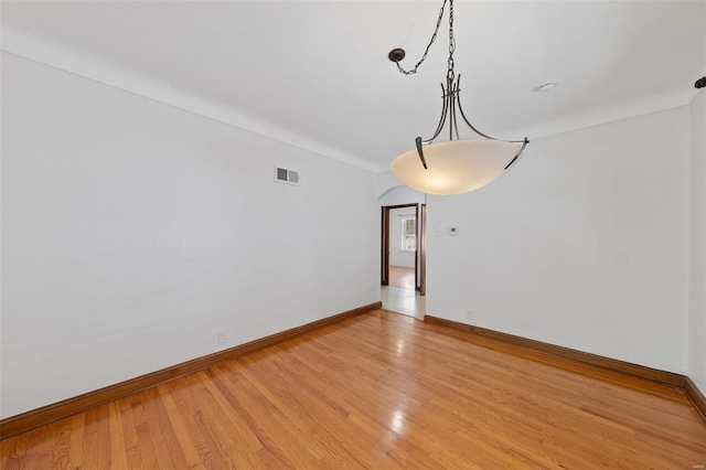 unfurnished room with visible vents, arched walkways, baseboards, and light wood-type flooring