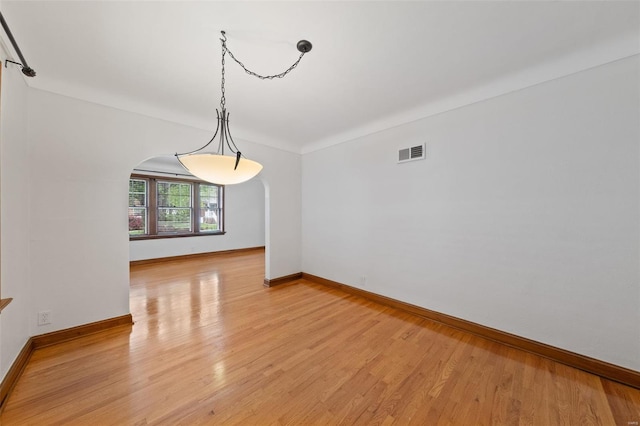 unfurnished dining area with arched walkways, baseboards, visible vents, and light wood-type flooring