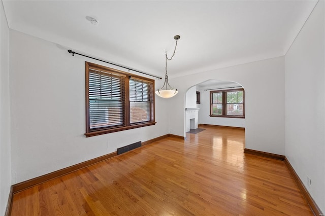 unfurnished dining area with arched walkways, baseboards, and light wood-type flooring