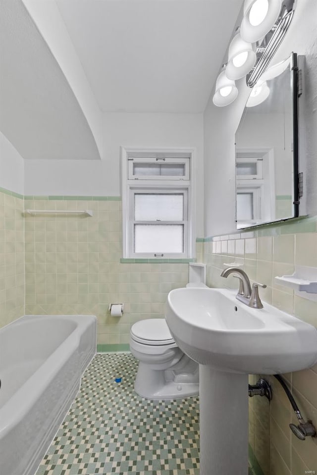 bathroom featuring wainscoting, a tub, toilet, and tile walls
