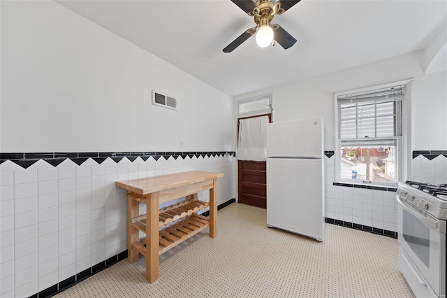 kitchen with a ceiling fan, visible vents, tile walls, wainscoting, and white appliances