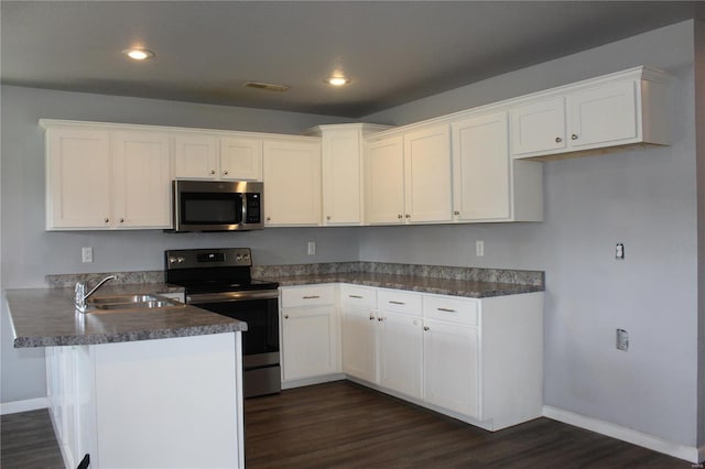 kitchen featuring a sink, a peninsula, dark wood-style floors, stainless steel appliances, and white cabinetry