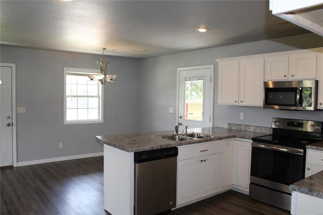 kitchen featuring an inviting chandelier, a sink, stainless steel appliances, a peninsula, and dark wood-style floors
